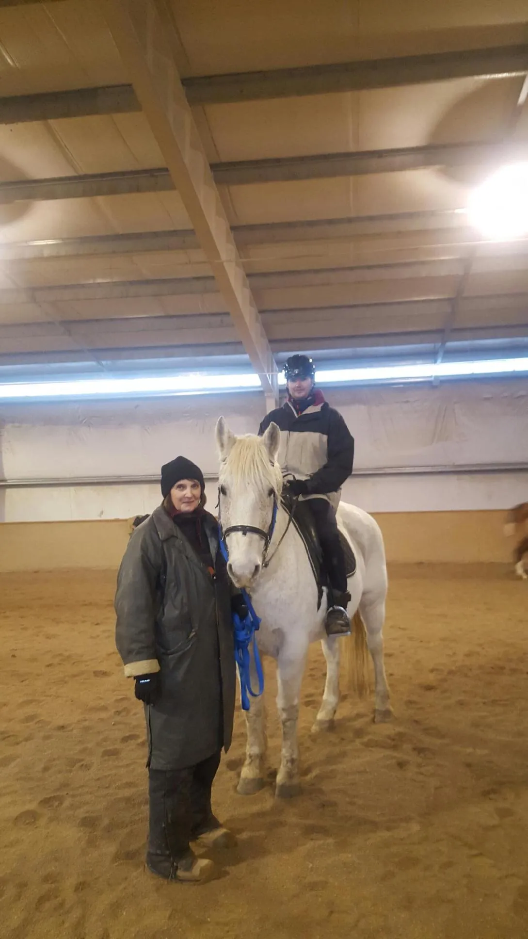Riding instructor standing alongside a rider on a white horse during an indoor arena lesson at Mountain View Ranch